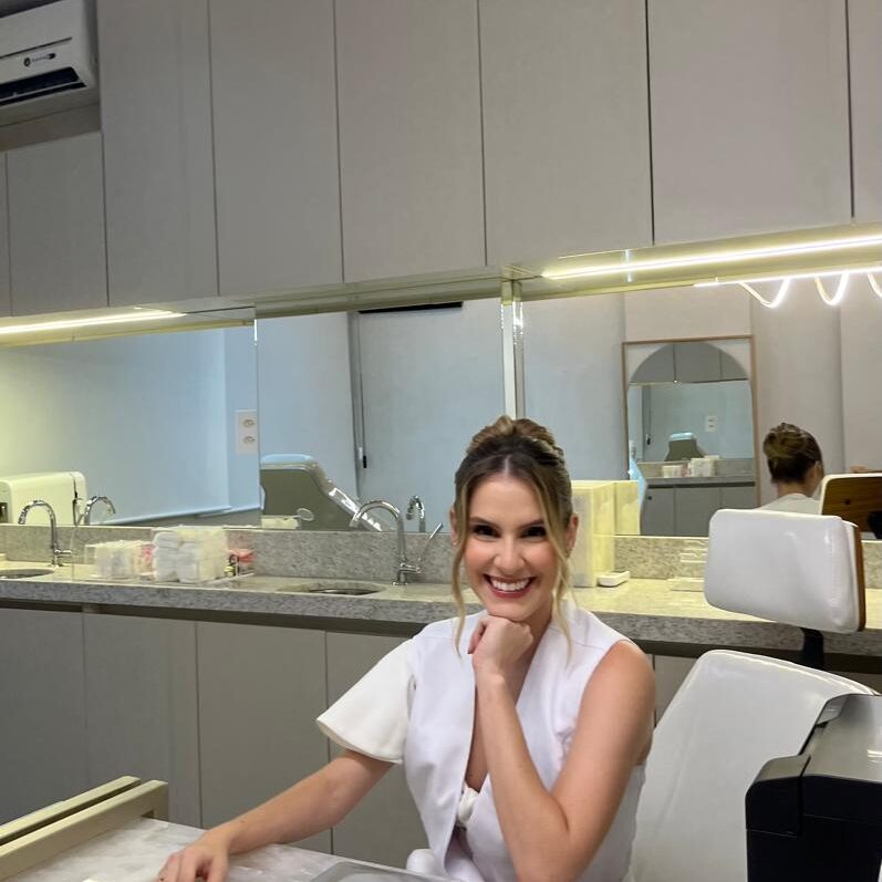 Dra. Marcela dermatologista e tricologista em Juiz de Fora está sorrindo em seu consultório moderno e aconchegante. Neste local ela trata queda de cabelo, rugas na face e faz preenchimento.